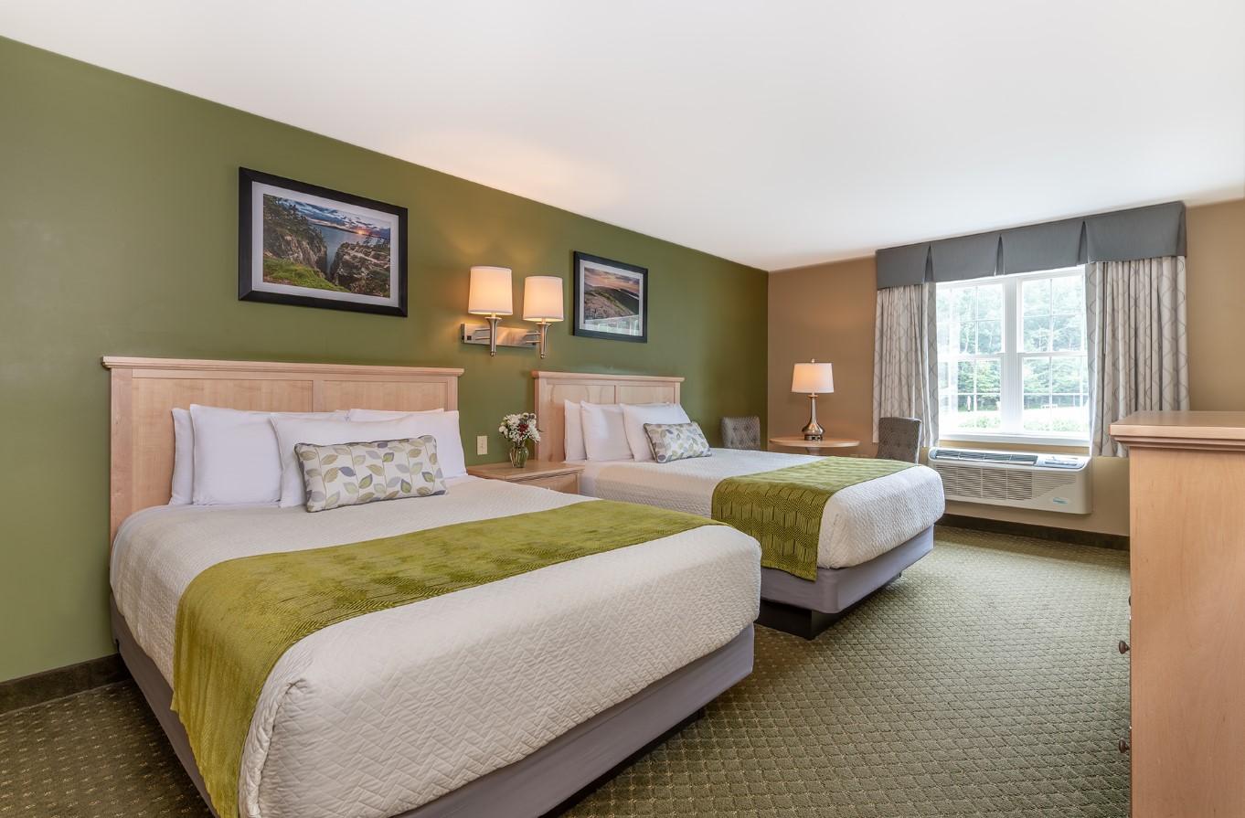 Two beds in a hotel room with green accents, a window, and framed pictures.