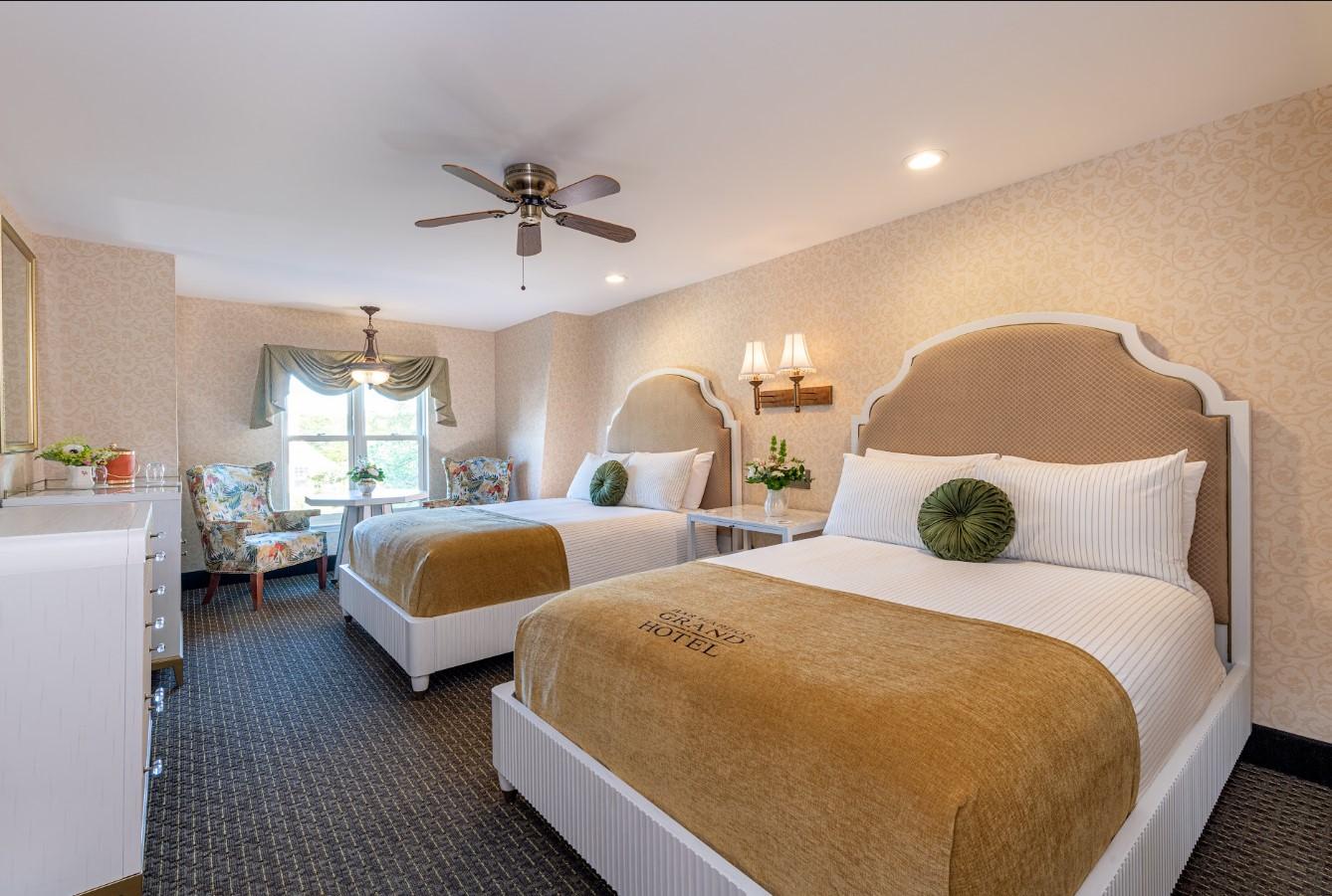 Two double beds in a bright hotel room with beige decor and green accents.