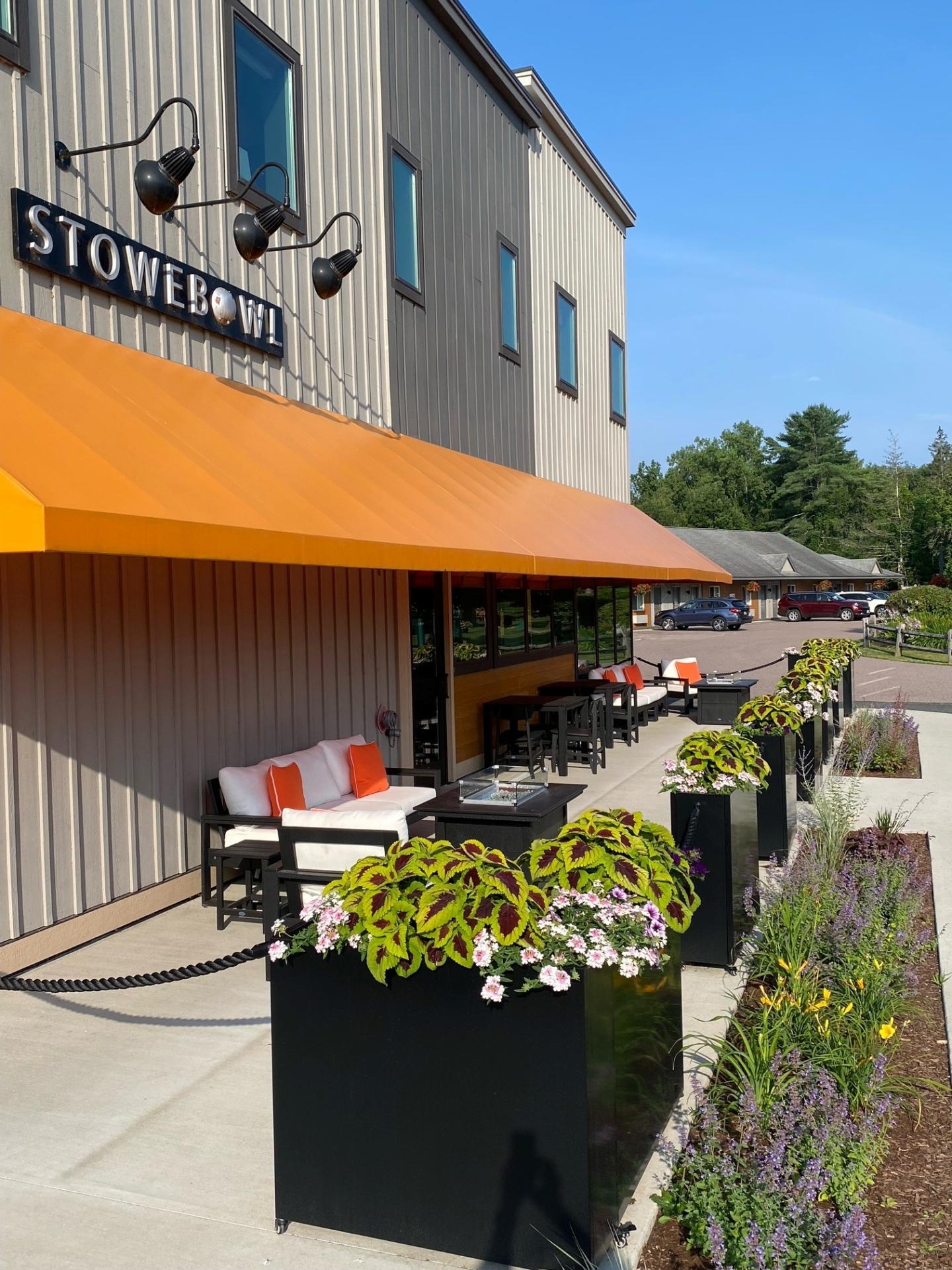 Outdoor patio with orange awning, seating, and flower planters on a sunny day.