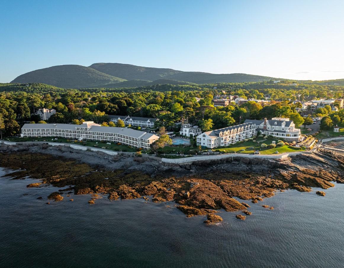 Coastal resort with rocky shore surrounded by trees and mountains in the background.