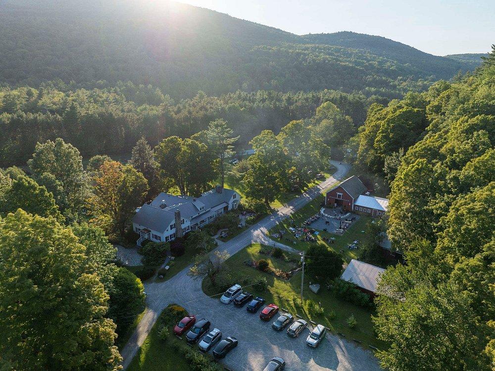 Aerial view of a rural landscape with trees, houses, and cars under sunlight.