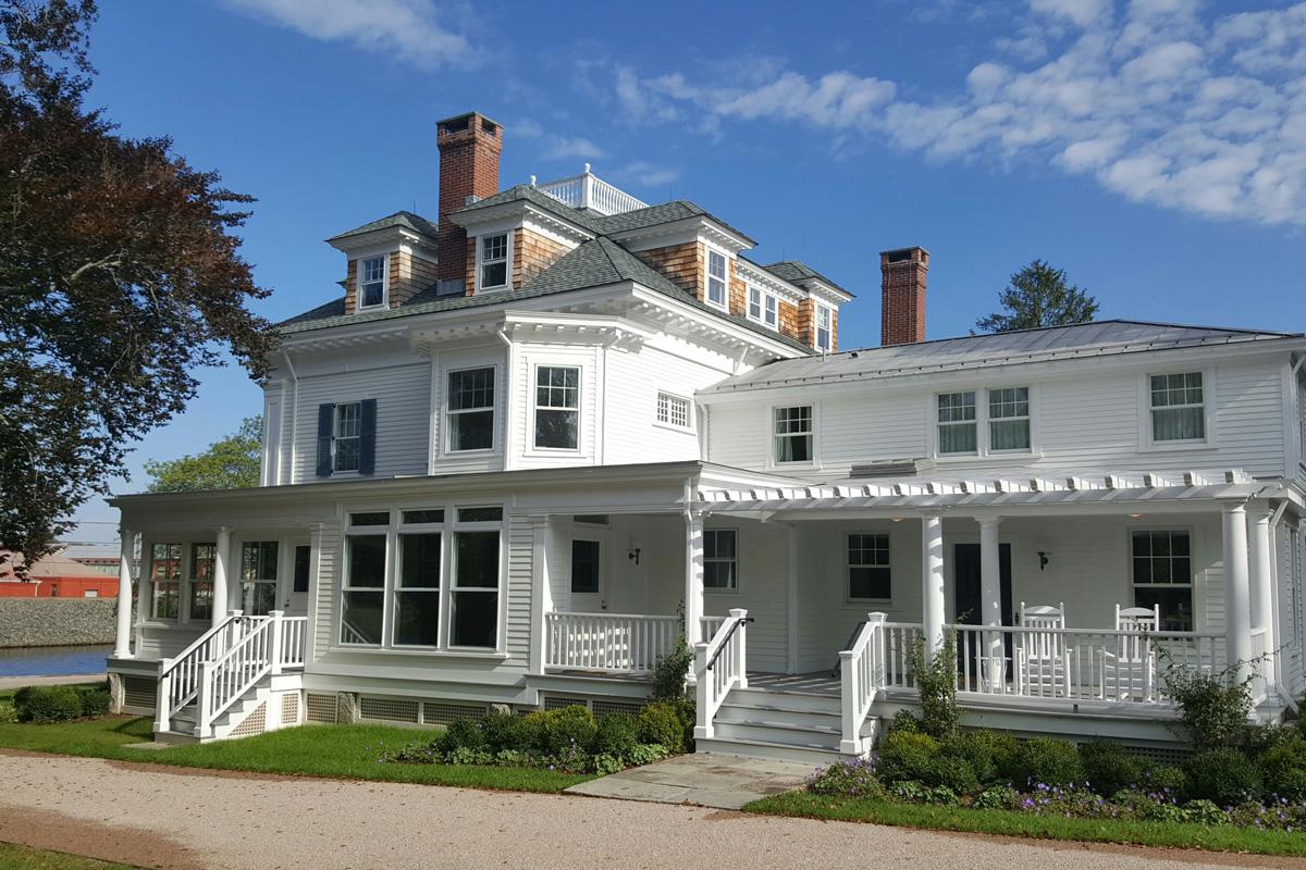 White colonial-style house with chimneys, set against a blue sky and green lawn.