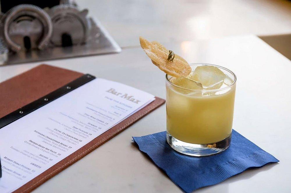 A yellow cocktail with ice and garnish on a blue napkin beside a menu.