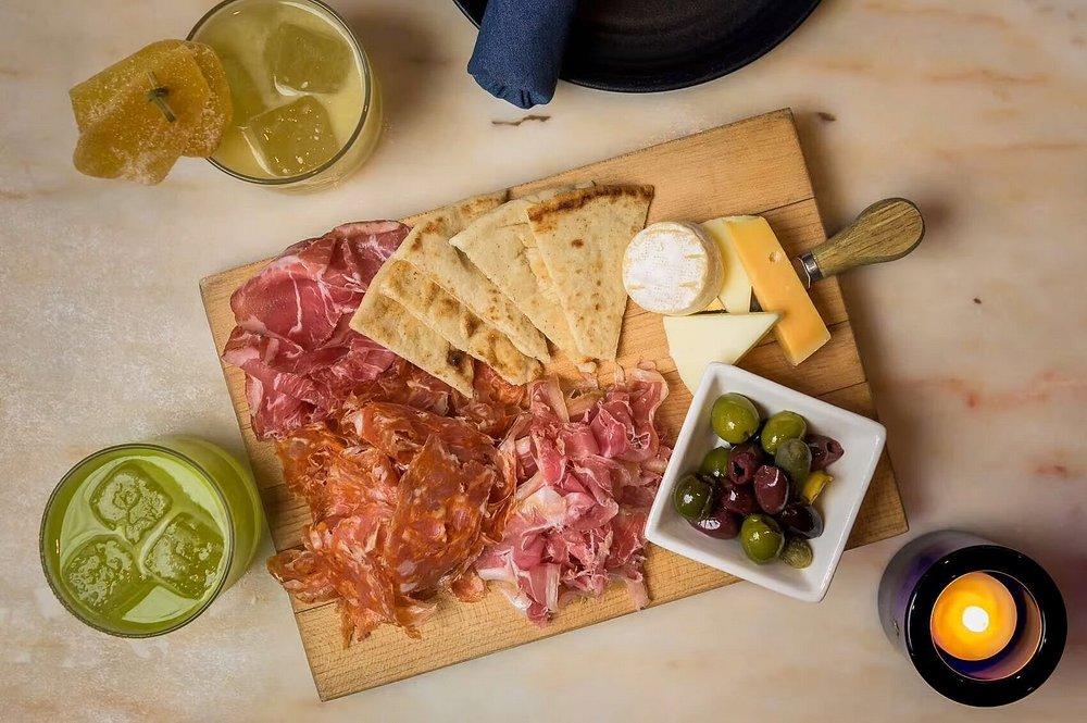 Charcuterie board with meats, cheese, bread, olives; drinks and candle nearby.
