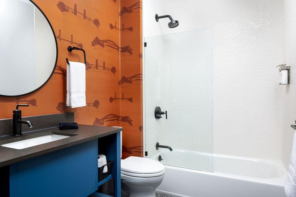 Modern bathroom with orange accent wall, round mirror, and glass shower door.
