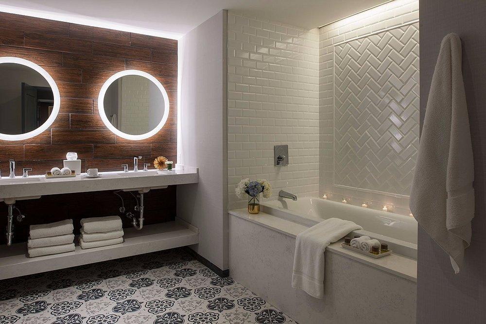 Modern bathroom with lit mirrors, white bathtub, and patterned floor tiles.