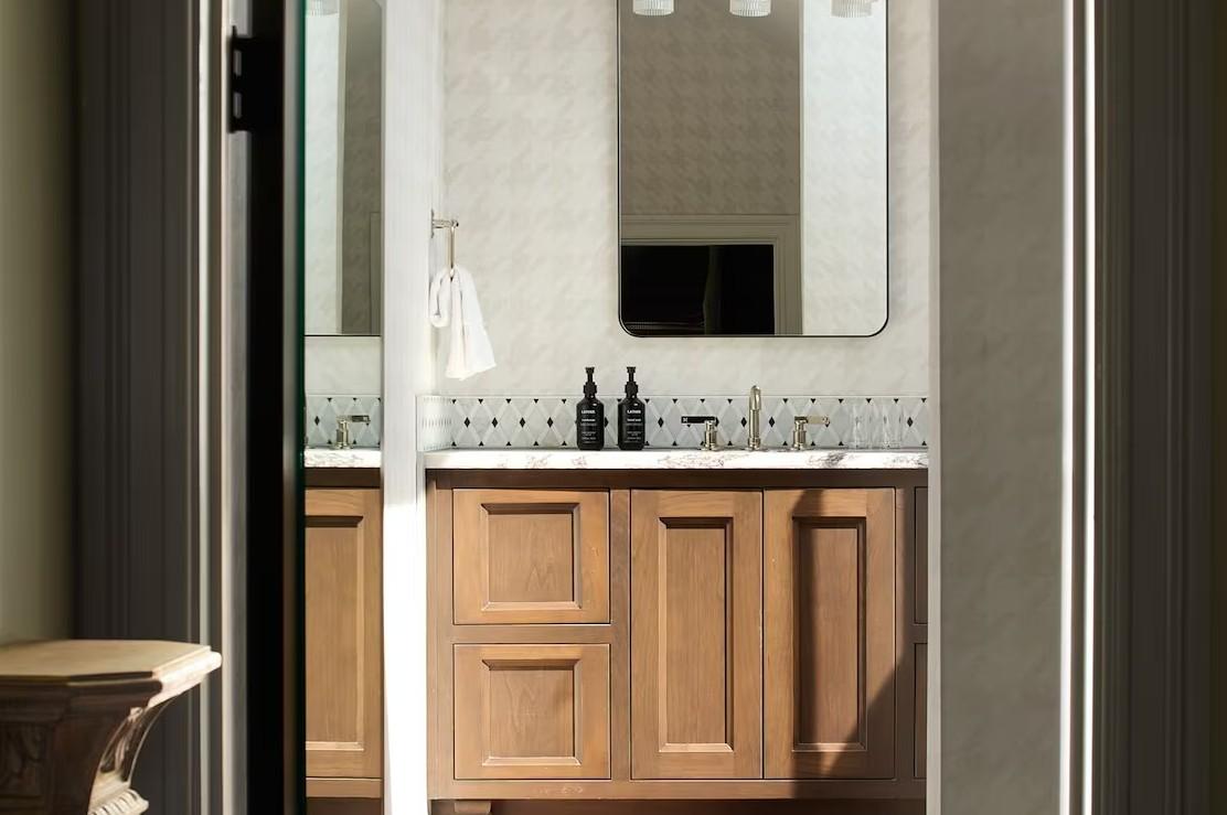 Bright bathroom with a wooden vanity, mirror, and glass bottles.