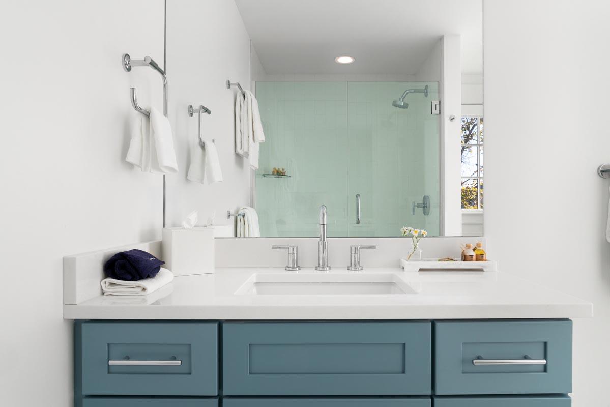 Modern bathroom with a blue cabinet, large mirror, and glass shower.