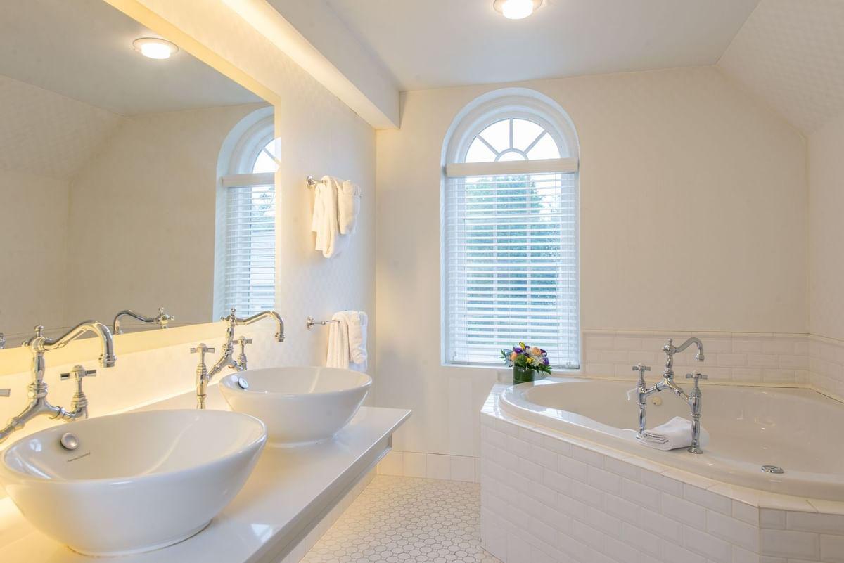 Luxurious bathroom with two sinks, large mirror, and corner bathtub. Bright natural light.