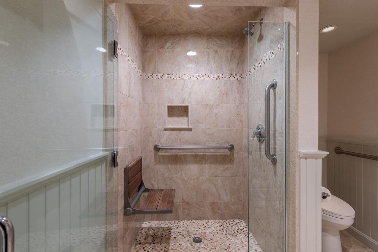 Walk-in shower with beige tiles, grab bar, and built-in wooden seat.