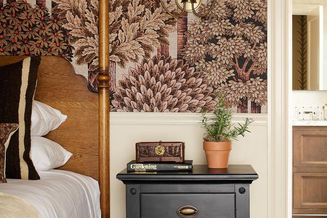 Bedside table with plant, book, tropical wallpaper.