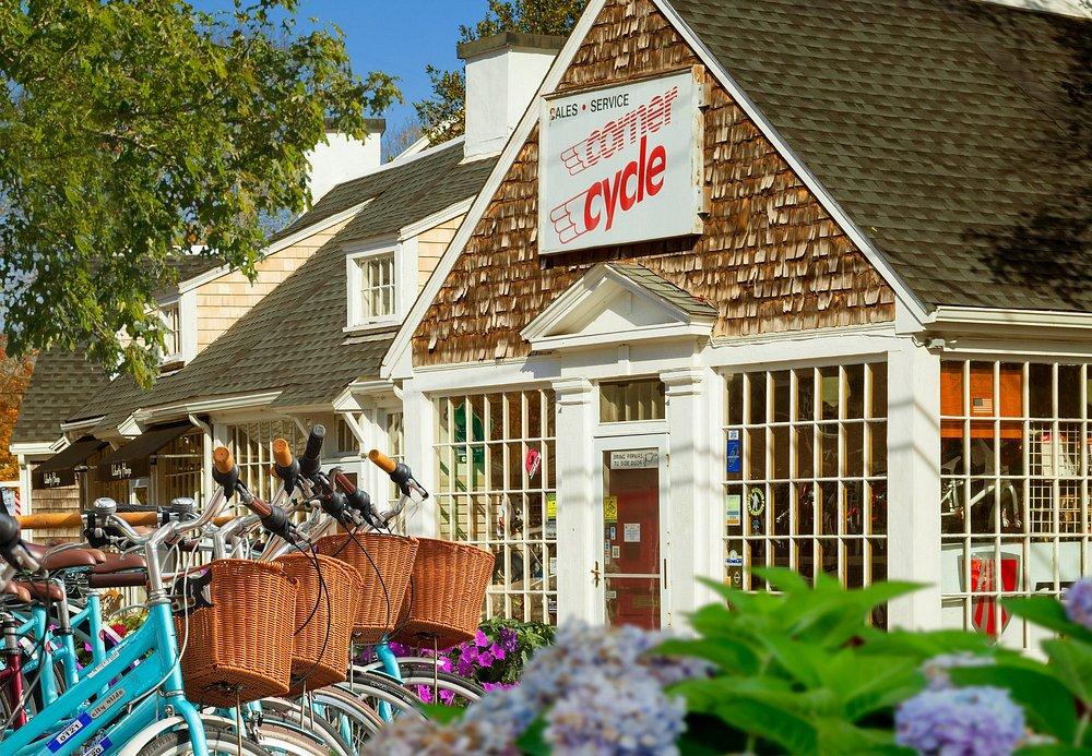 Bicycles with baskets parked outside a rustic cycle shop.