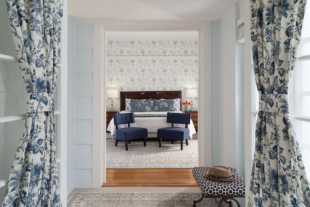 Elegant bedroom with blue floral wallpaper, two navy chairs, and patterned curtains.