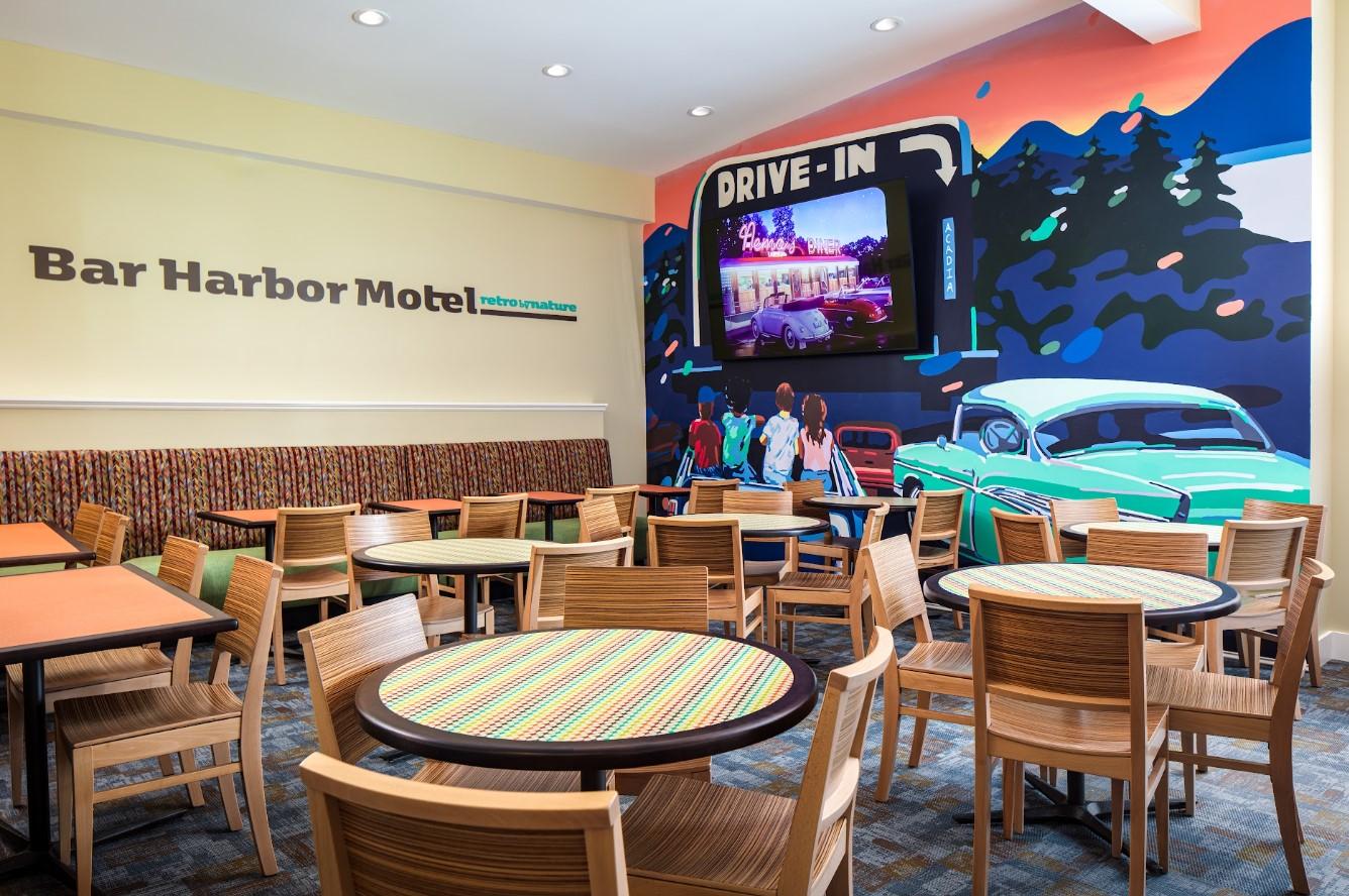Café area with tables, chairs, and a colorful mural of a drive-in.