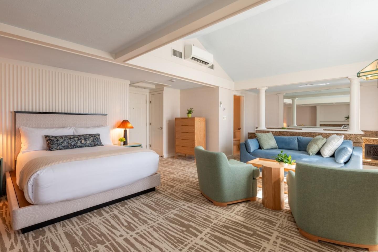 Cozy hotel room with bed, blue sofa, green chairs, and wooden furniture.