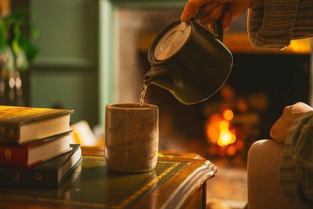 Cozy setting with tea being poured by a fireplace.