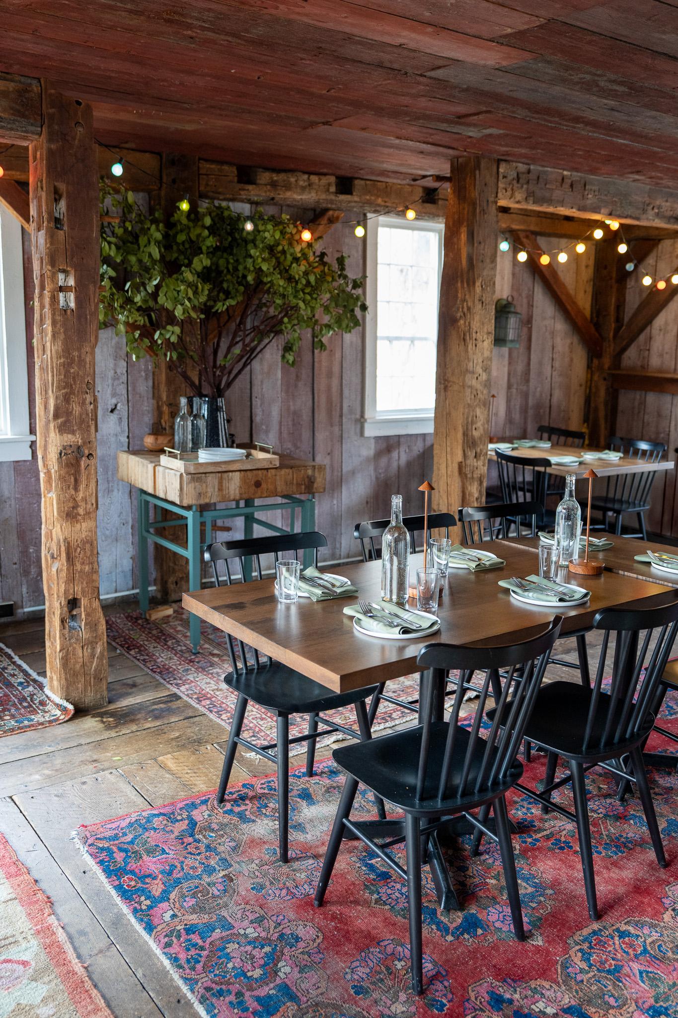 Rustic dining area with a wooden table, black chairs, and colorful rugs.