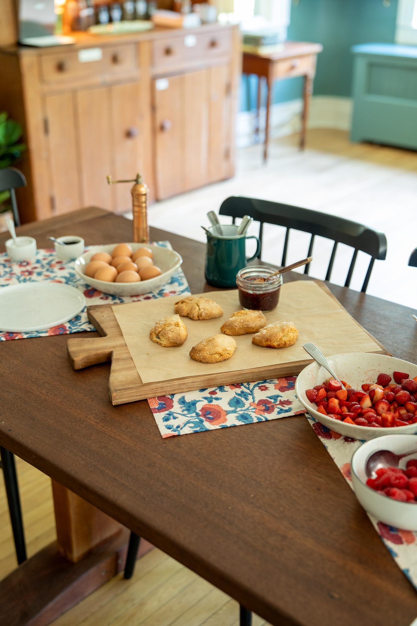 Pastries, jam, and fruit on a wooden table in a cozy inn parlor for a complimentary breakfast.