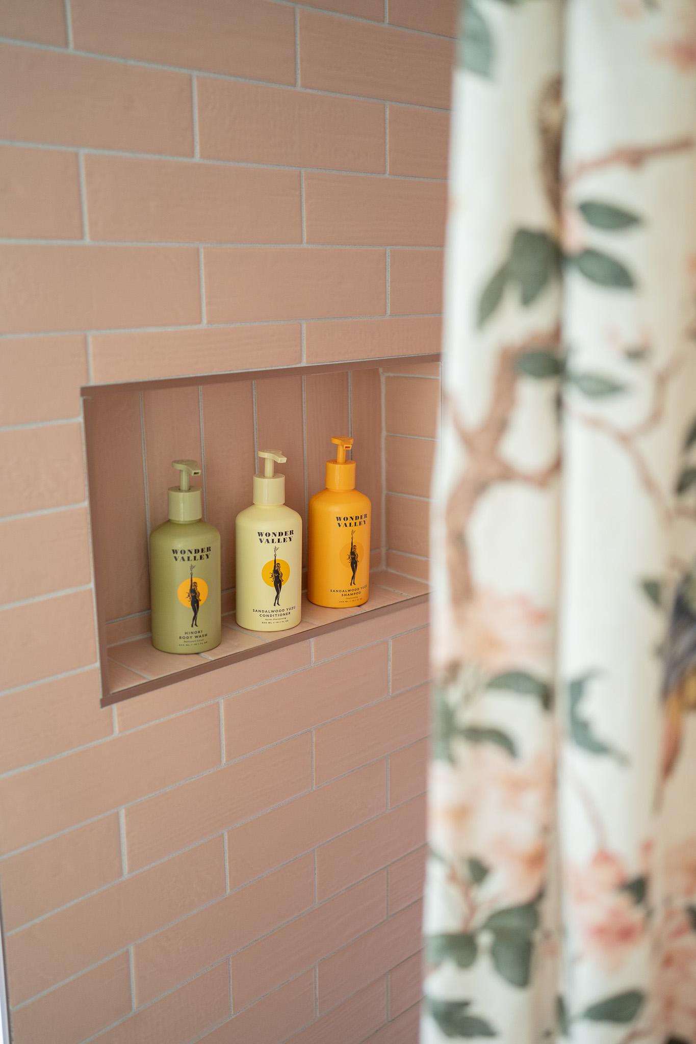 Soap dispensers in shower niche with floral curtain.