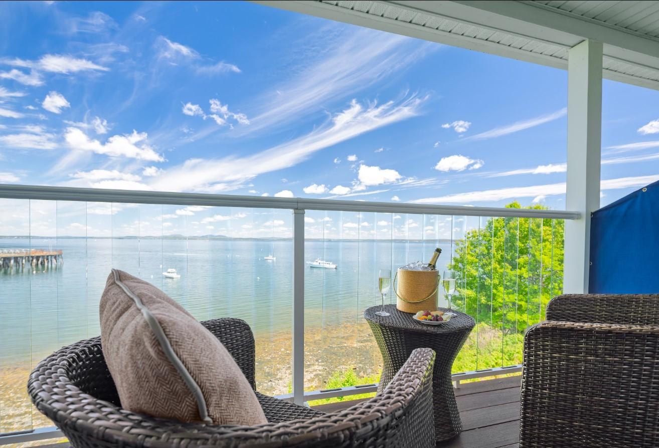 Coastal balcony with wicker chairs, calm sea view, and blue sky.