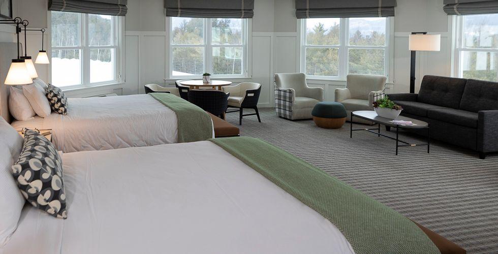Spacious hotel room with two beds, sofa, and large windows.