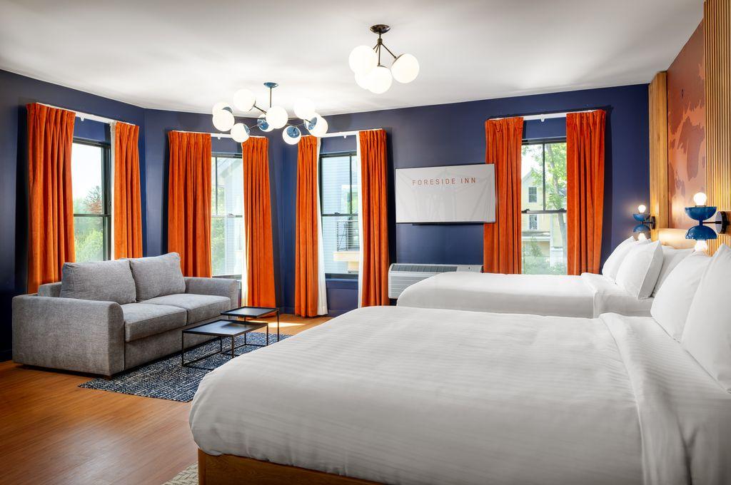 Hotel room with two beds, orange curtains, and a gray sofa.