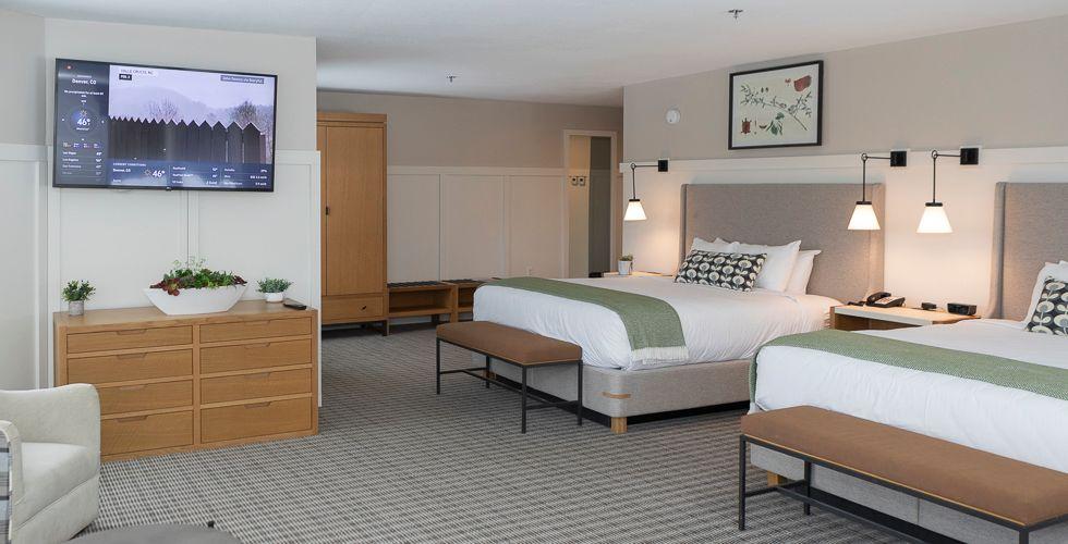 Modern hotel room with two beds, wall-mounted TV, and minimalist decor.