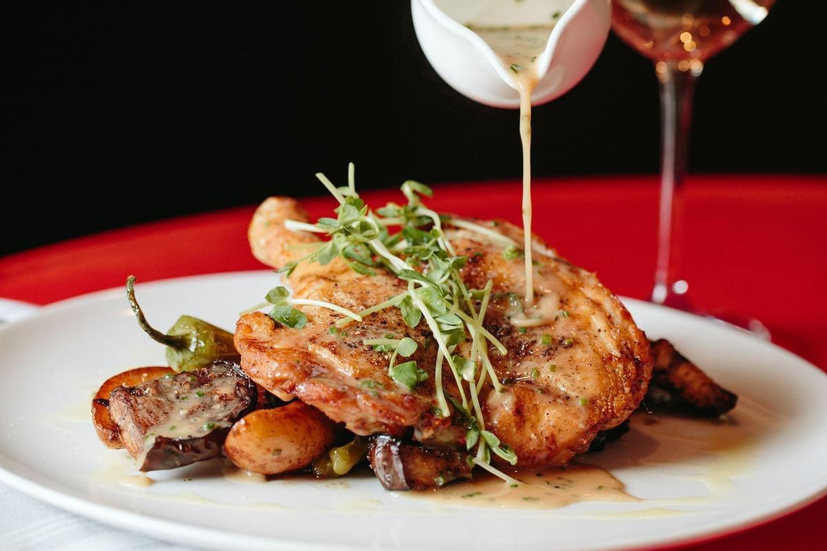 Roasted chicken with potatoes, sauce, and greens on a white plate.