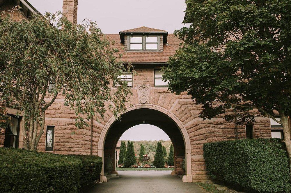 Stone archway with trees and greenery on both sides. House visible in background.