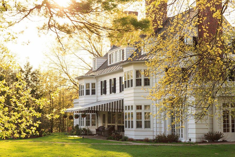 White house with large windows, surrounded by sunlit trees in spring.