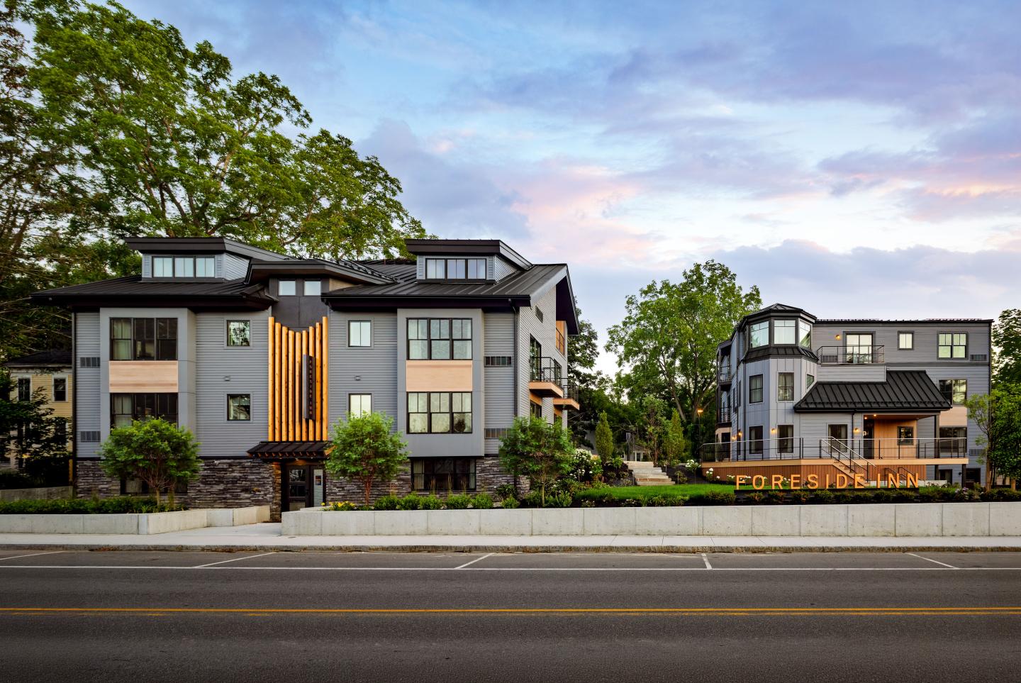 Modern buildings with large windows and trees in the background at sunset.