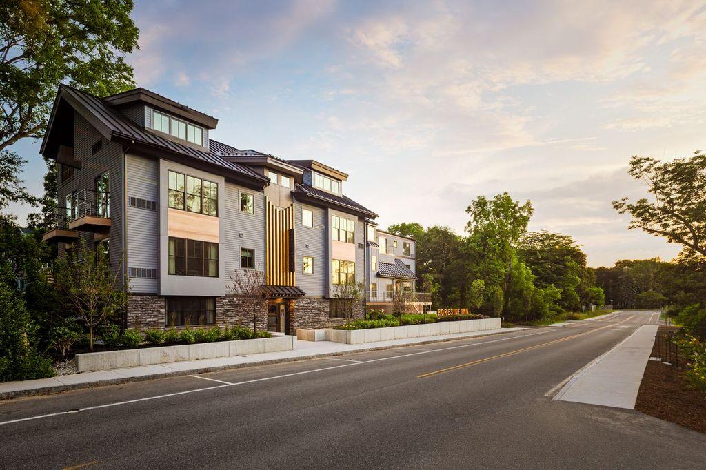 Modern townhouse complex beside a quiet tree-lined street at sunset.