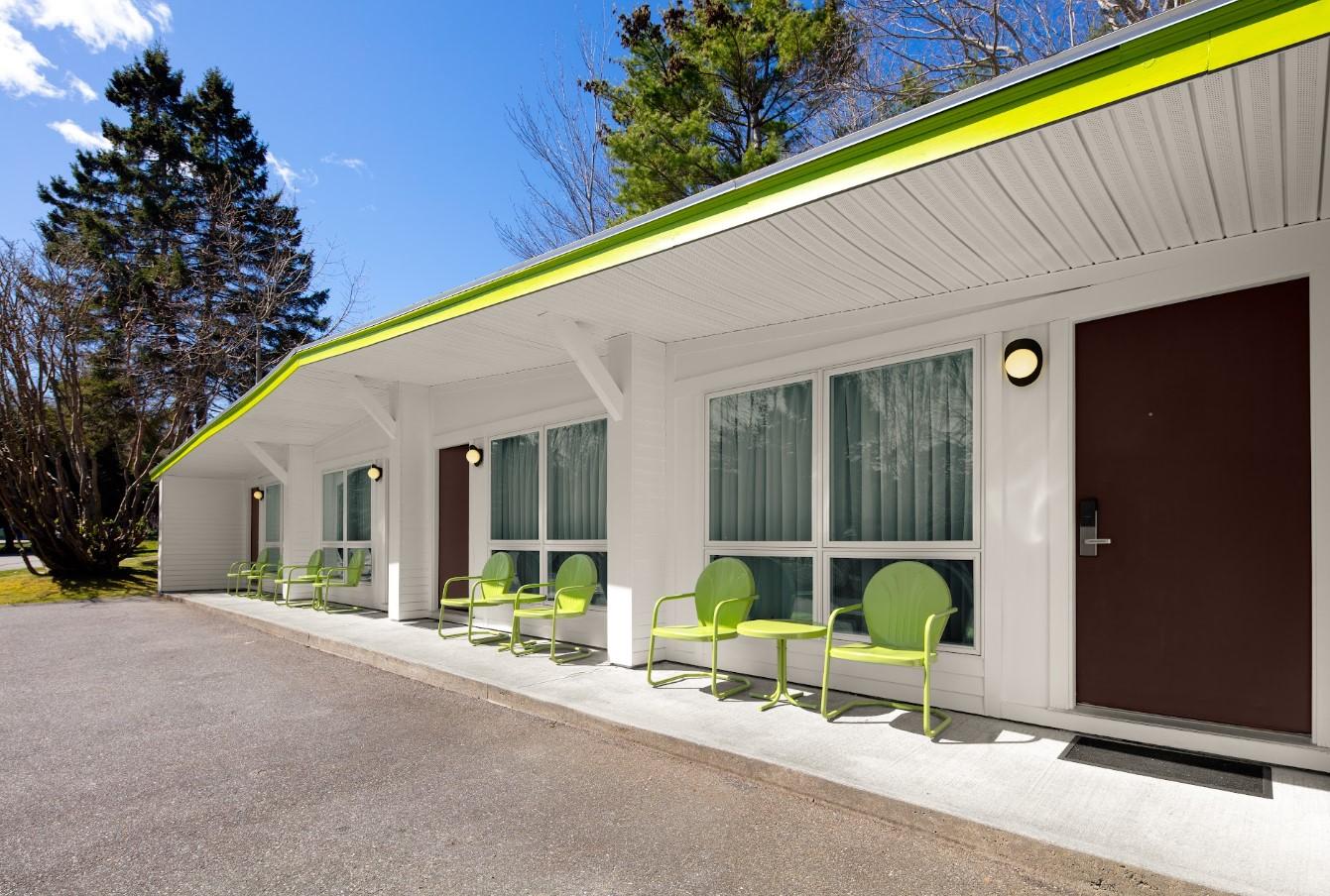 White motel exterior with green chairs and a yellow-trimmed roof.