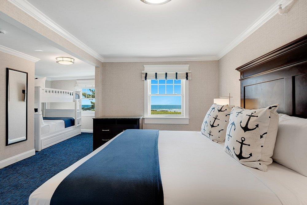 Cozy hotel room with a king bed, nautical-themed pillows, and bunk beds in an adjoining area.