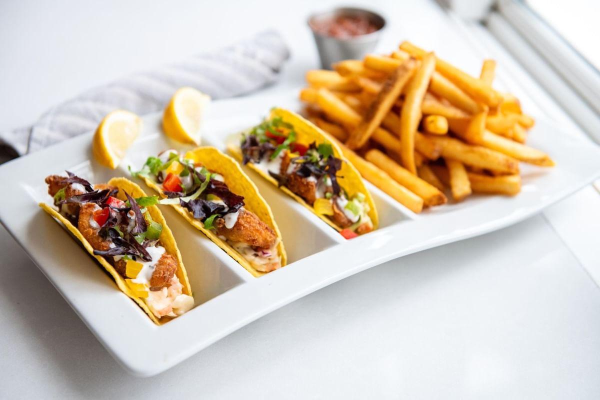 Fish tacos with fries and lemon on a white plate.
