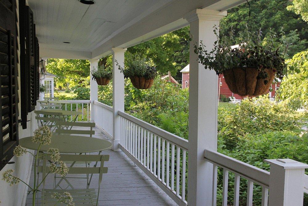Veranda with hanging plants, white railing, green chairs, overlooking lush garden.