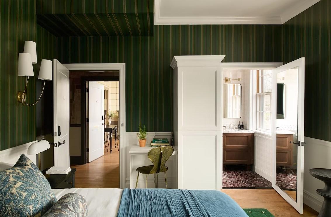 Bedroom with green striped walls, white furniture, and open doors to a bathroom.