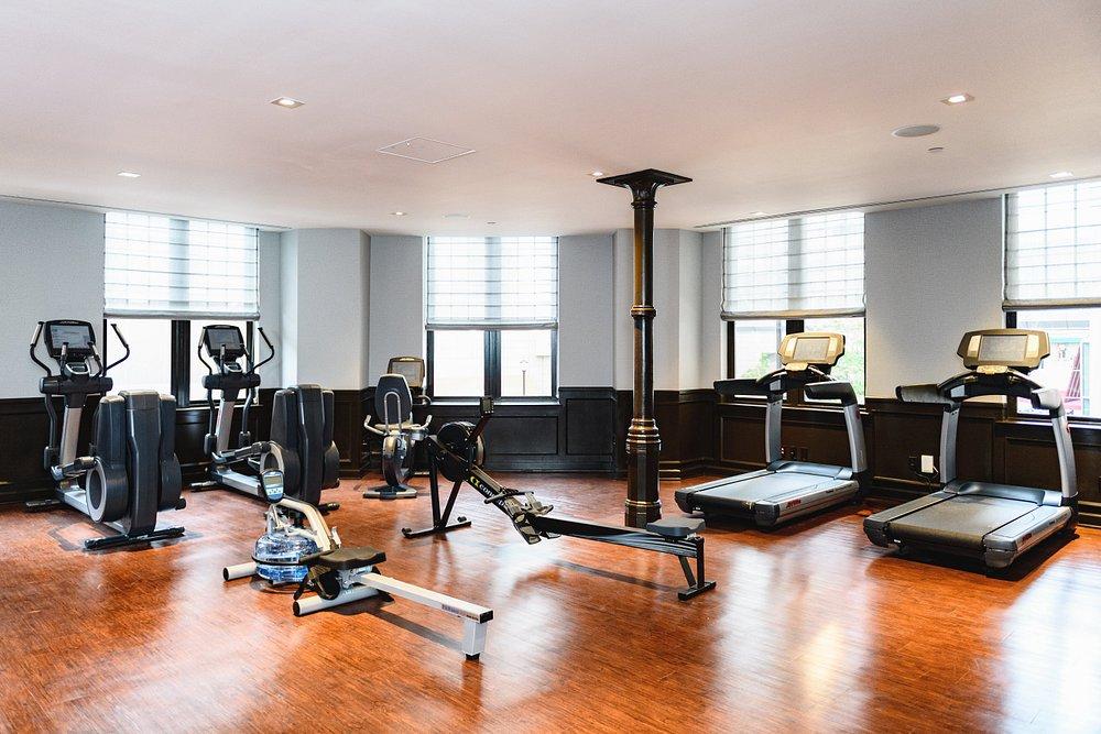 Bright gym with treadmills, exercise bikes, and a rowing machine on wooden flooring.