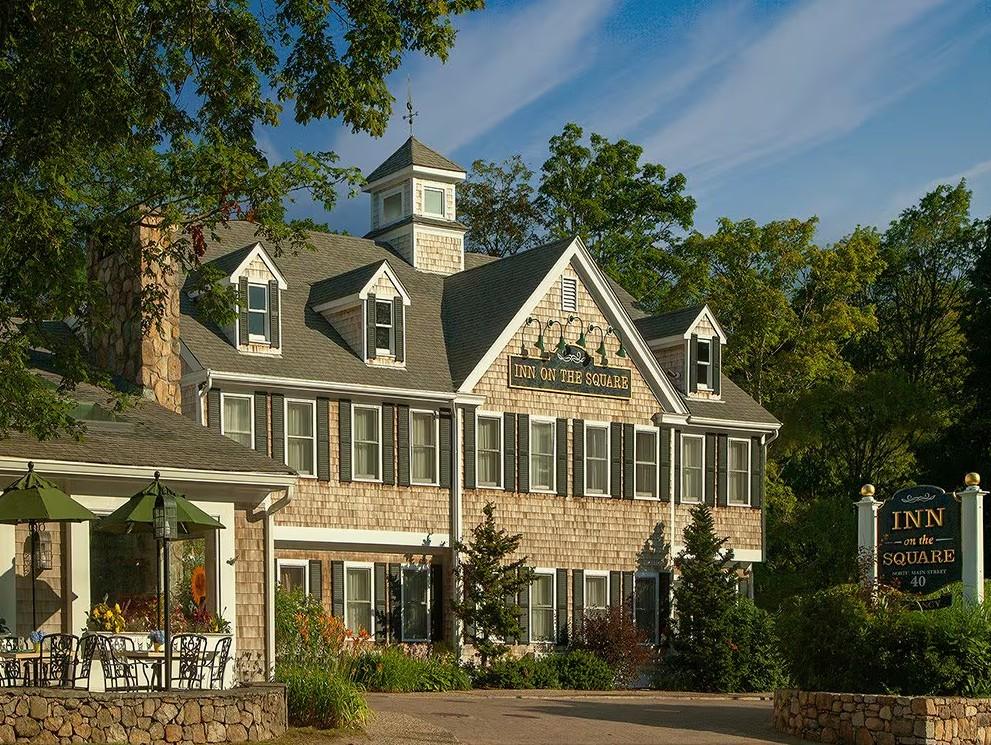 Historic inn with stone facade, surrounded by trees under a blue sky.