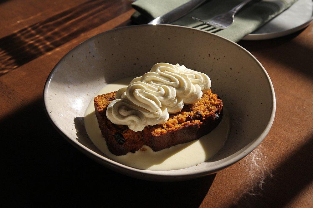 Carrot cake slice with cream topping in a bowl, fork and napkin nearby.