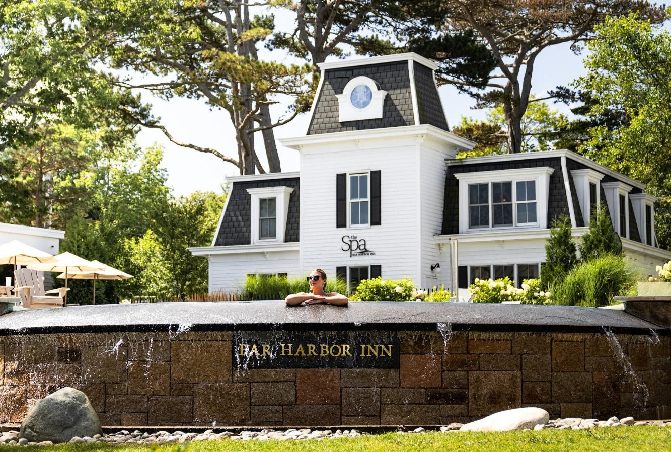 White inn with a black roof behind a fountain and trees.