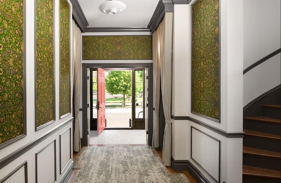 Elegant hallway with green patterned walls, open door, and a view of trees outside.