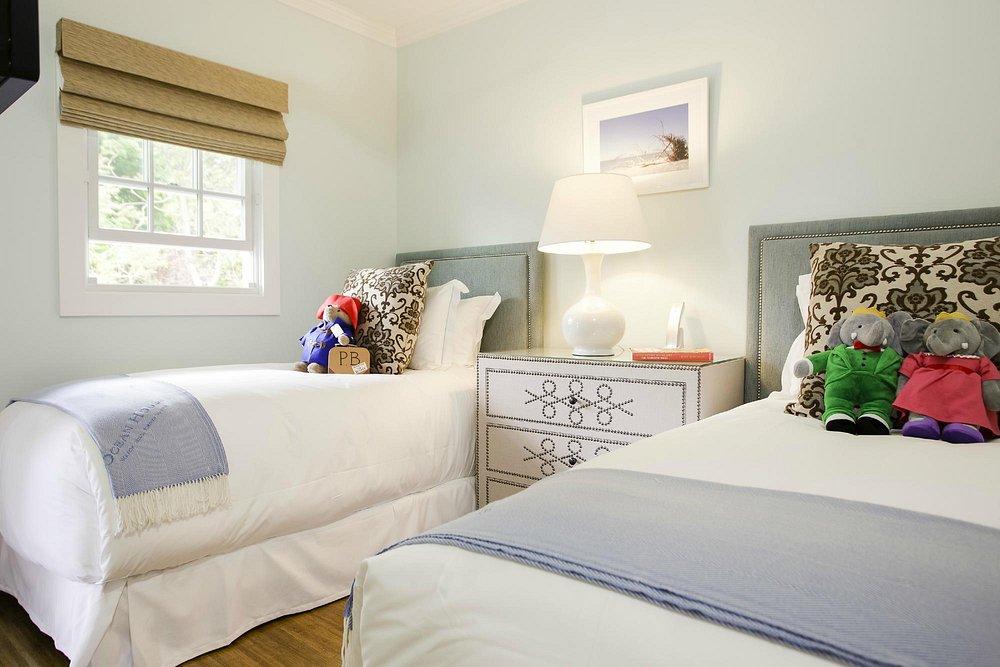 Two twin beds in a bright room with plush toys and a bedside lamp.