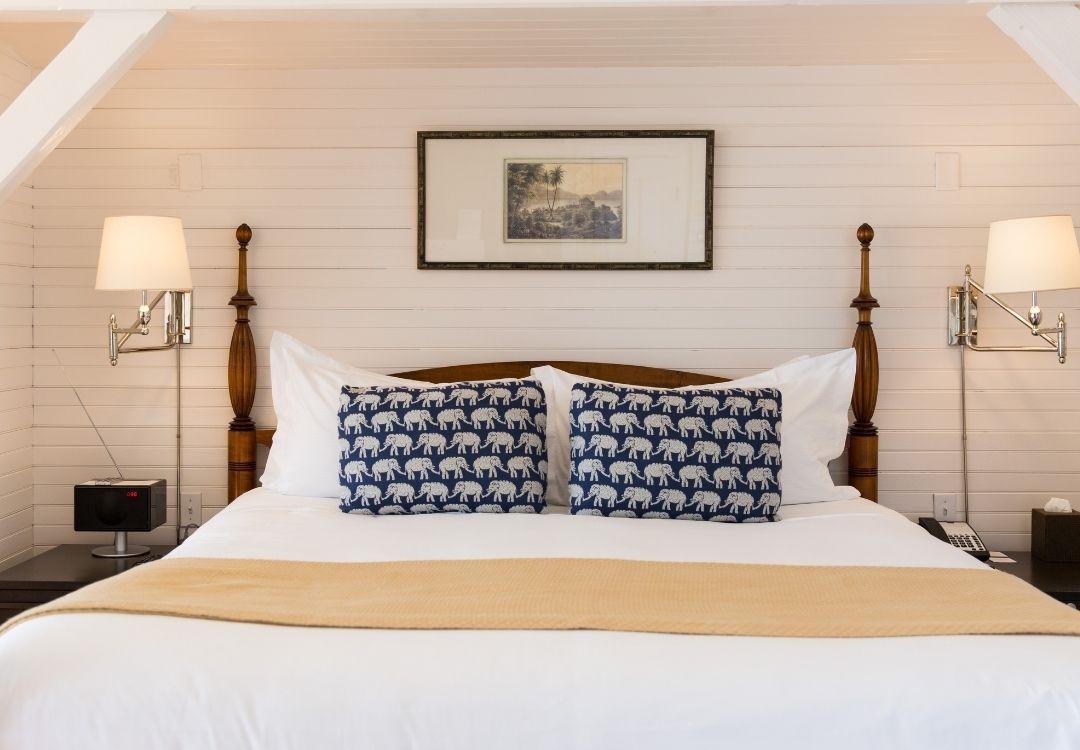 A neatly made bed with two patterned pillows, flanked by lamps, in a cozy white room.