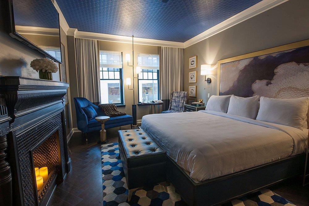 Stylish hotel room with a king bed, blue accents, and a lit fireplace.