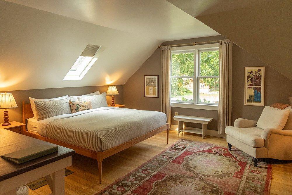 Cozy attic bedroom with a large bed, armchair, and window with garden view.