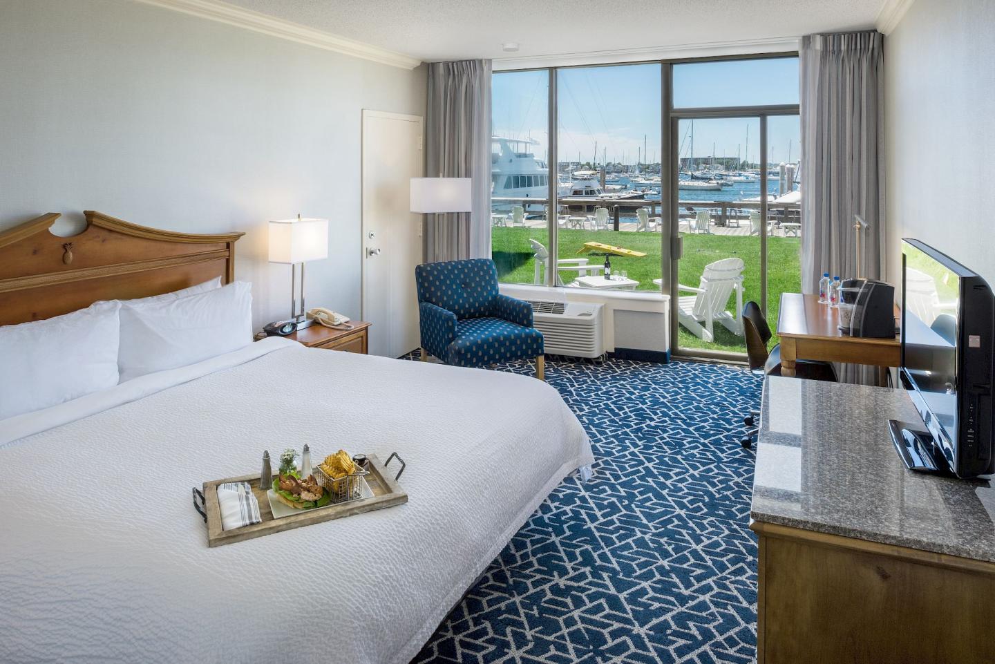 Contemporary hotel room with ocean view, large bed, tray of food, and blue-patterned carpet.