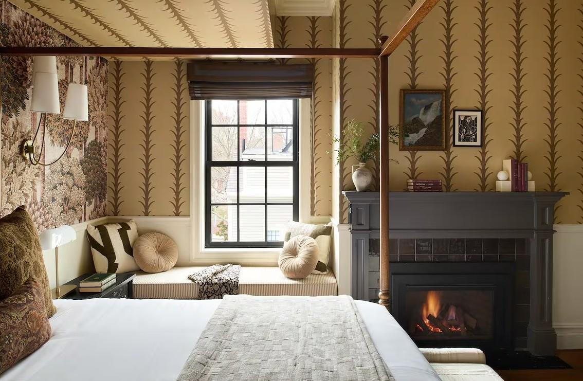 Cozy bedroom with a fireplace, patterned wallpaper, and window seat.