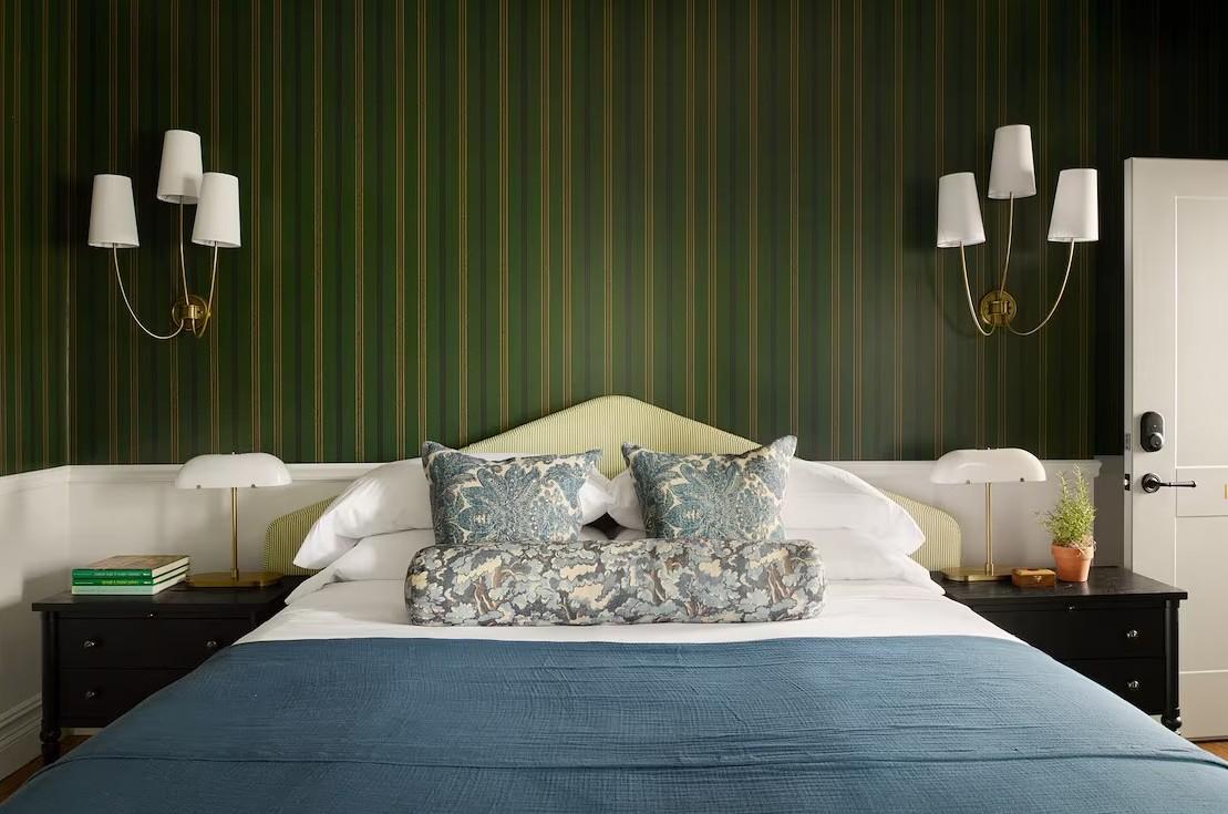 Stylish bedroom with green-striped walls, blue bedspread, and floral cushions.