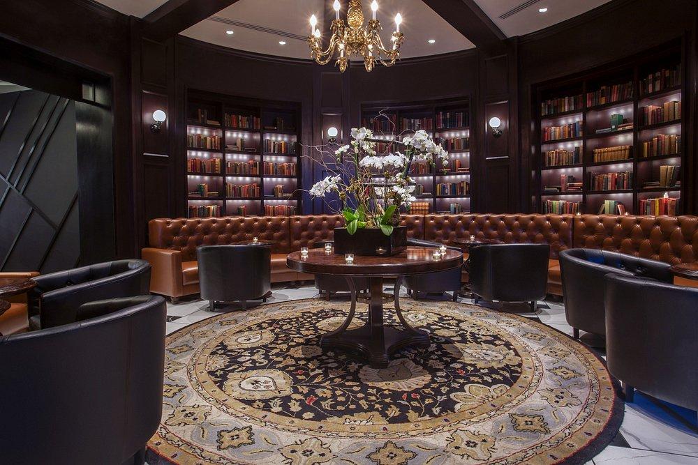 Luxurious library with leather chairs, a round table, bookshelves, and a chandelier.
